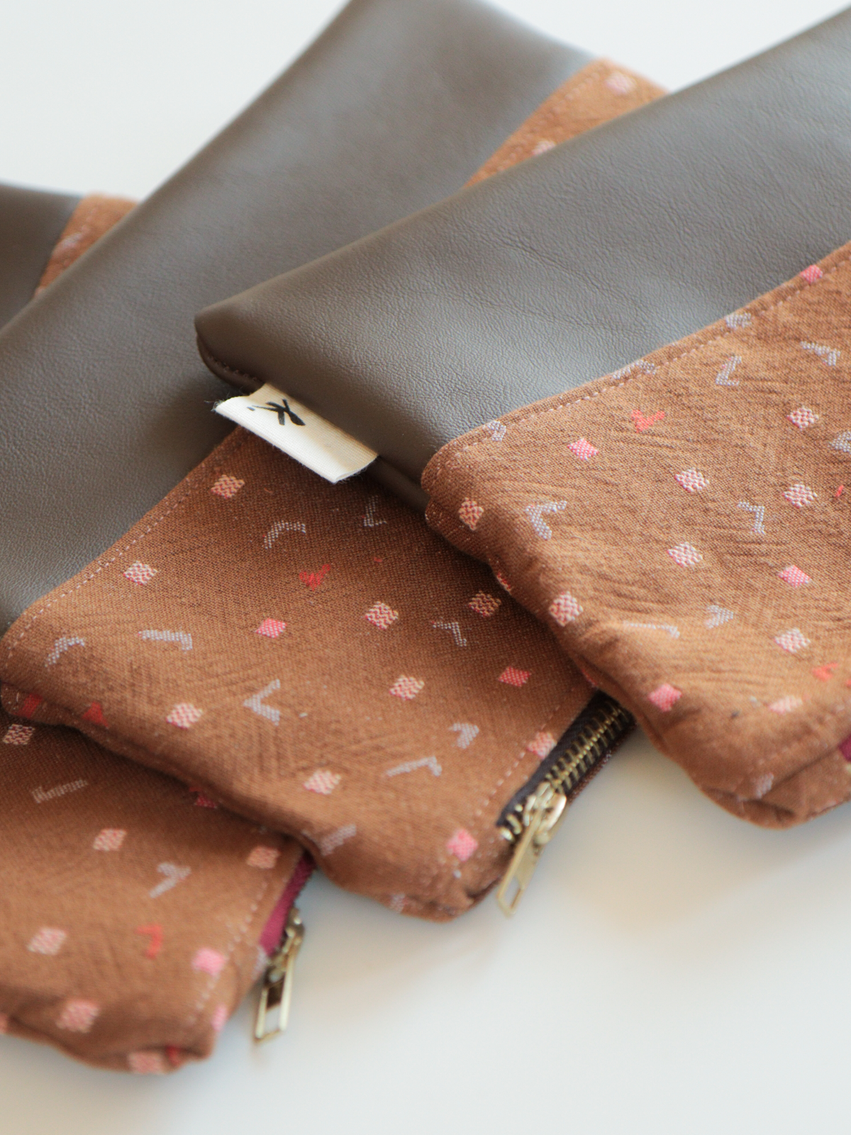Dettaglio degli astucci pochette Terracotta in tessuto fantasia marrone e pelle, con chiusura a zip metallica
